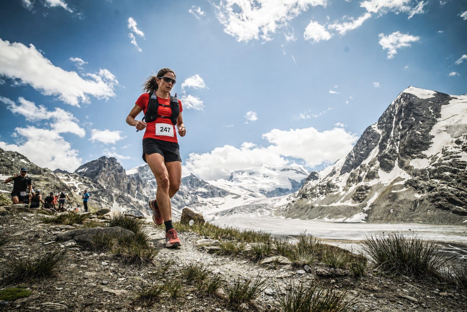 A trail runner descending below snowy peaks